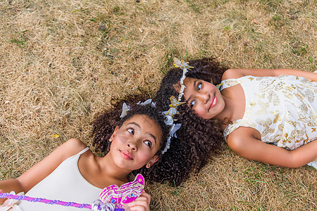 两个女孩打扮成仙女头挨头躺在草地上图片