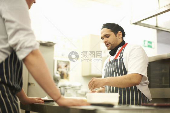 在厨房柜台为十几岁的餐饮学生展示食品准备的厨师讲图片