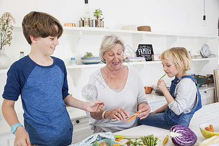 高龄妇女和孙子孙女在厨房餐桌上准备蔬菜图片