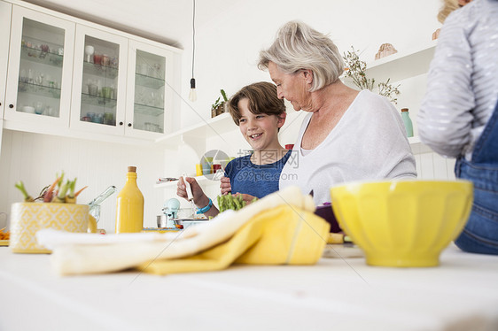 高龄妇女和孙子在厨房餐桌上准备蔬菜图片