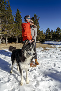 带狗的成年夫妇在雪覆盖的森林中背景图片