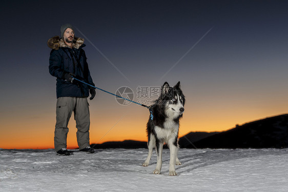 成年男子与狗一起在夜间下雪图片