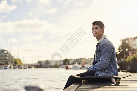 坐在河边滑板旁的年轻人英国布里斯托尔图片