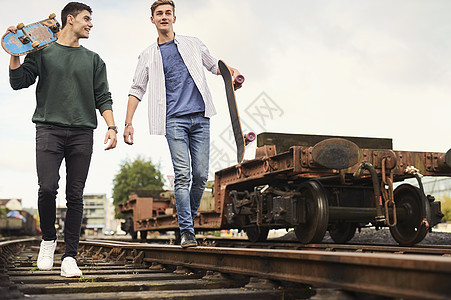 2名青年男子在火车轨道上拿着滑板行走英国布里斯托尔图片