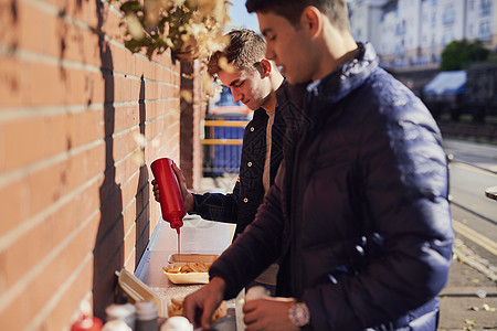 2名青年男子在外卖食品摊物上加番茄酱图片