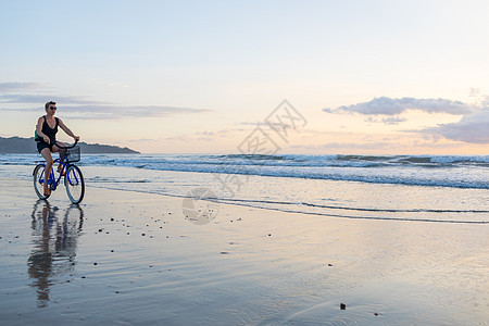 日落海滩骑自行车的女人图片