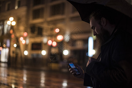 成年人晚上在城市散步使用雨伞看智能手机的男人图片