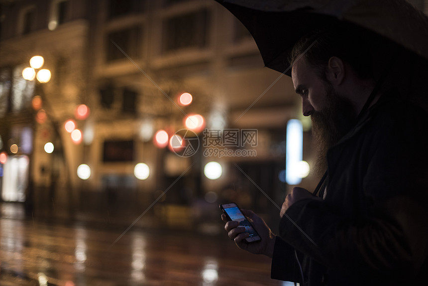 成年人晚上在城市散步使用雨伞看智能手机的男人图片