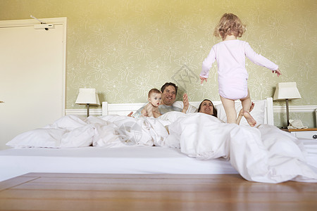 蹒跚学步的女婴与父母和小弟弟在床上图片