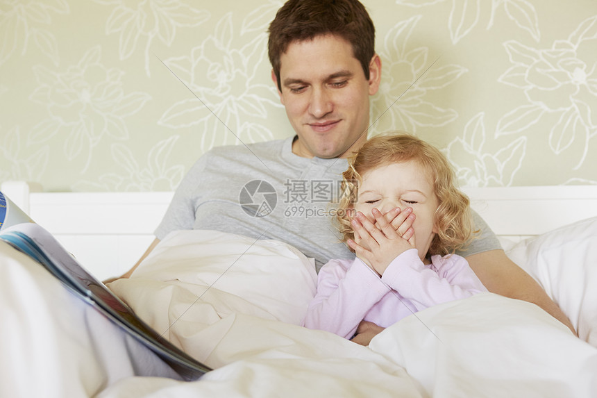 与父亲在床上打哈欠的女幼儿图片