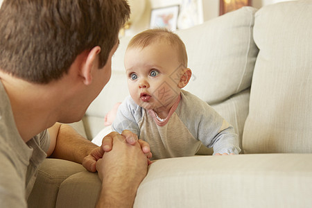 沙发上可爱的蓝眼睛女婴盯着她父亲看图片