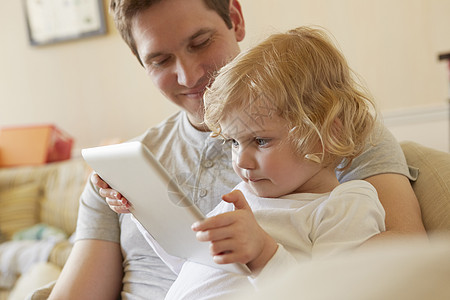 坐在沙发上使用数字平板电脑的父亲和女幼儿图片