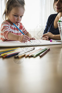 坐在桌边的女幼儿母亲在草图本上绘画图片