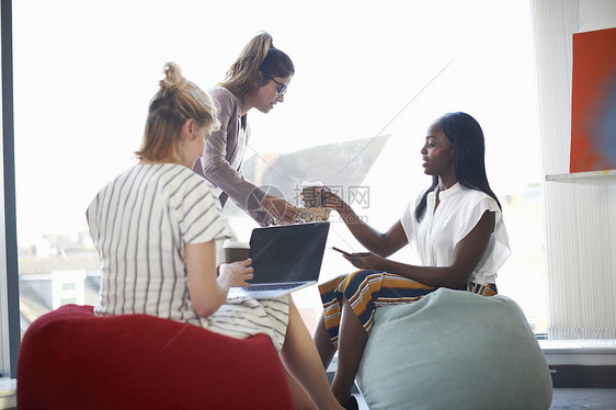 妇女向坐在豆袋上的女商人提供咖啡图片