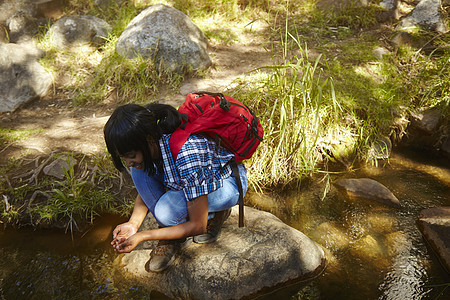 女青年徒步旅行蹲在河边的岩石上南非开普敦图片
