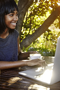 坐在户外使用笔记本电脑喝咖啡的年轻妇女图片