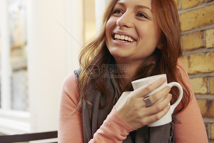 坐在户外拿着咖啡杯微笑的年轻女子图片