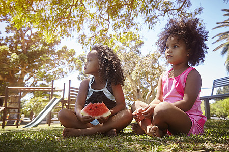 两个年轻的姐妹坐在草地上吃西瓜图片