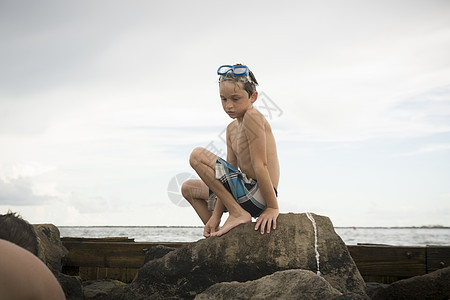 海岸岩石上蹲着的男孩在沉思图片