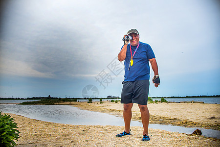 成熟男子站在海滩上透过摄像机寻找图片