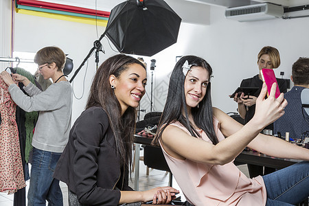 两个时装模特在摄影演播室使用智能自拍手机图片