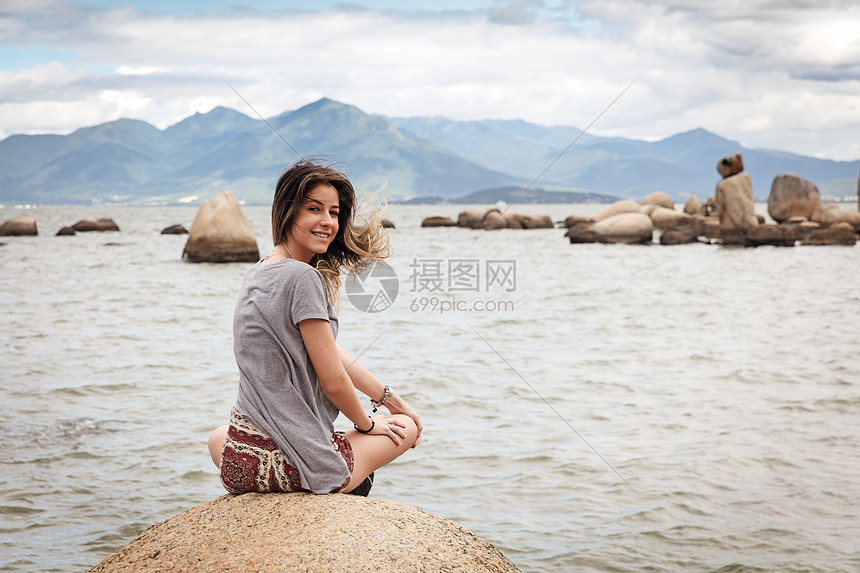 坐在岩石上回头看着镜头微笑的少女图片