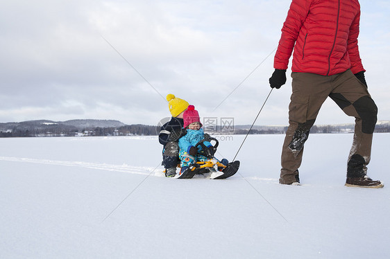 父亲拉着坐着两个孩子的雪橇图片