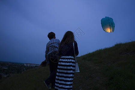 一对夫妇在黄昏时草地上行走看着空中的天灯图片