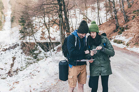 在雪林路上徒步旅行的情侣看着智能手机图片