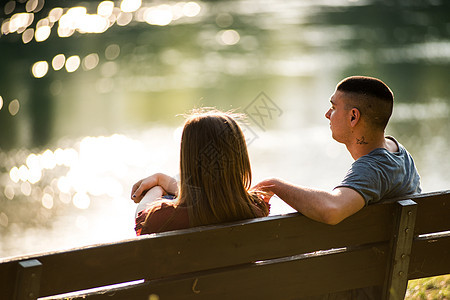 情侣坐在河边的长椅上的背影图片