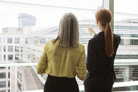 两个商业女人站在办公室的窗口前图片