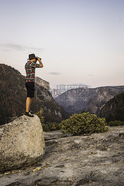 美国加利福尼亚州约塞米特公园里站在巨石上拿望远镜远望的男人图片