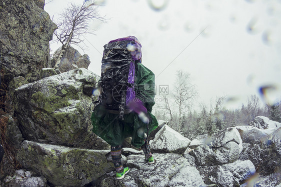 身穿防水衣的女徒步旅行者者在雪暴中蹲在岩石上图片