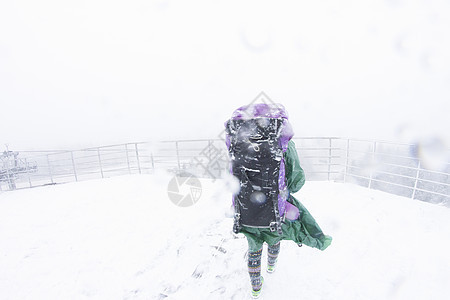 在雪暴中走在山上女徒步旅行者背影图片