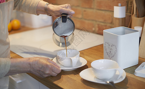 老年妇女将咖啡倒进杯子图片