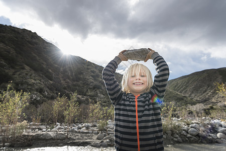 可爱男孩的肖像从河床抱起岩石图片