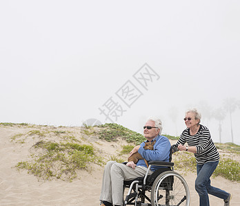 沙丘上给丈夫推轮椅的老年妇女图片