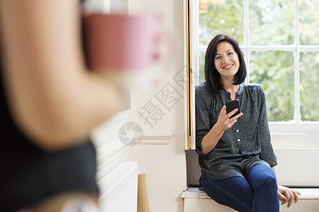 创意工作室窗边座位上拿着手机微笑的女设计师图片