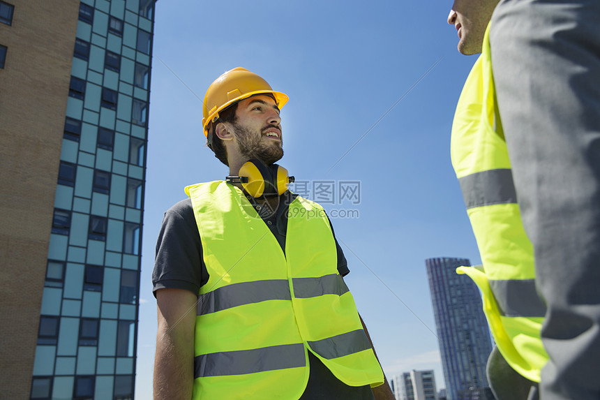 两个男人戴着安全帽穿着背心在户外交谈图片