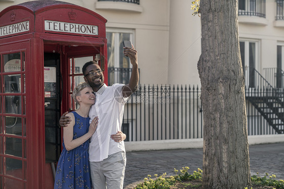 年轻夫妇站在红色电话箱旁边抬头微笑图片