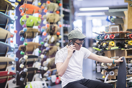 年轻男滑板运动员在店打智能电话图片