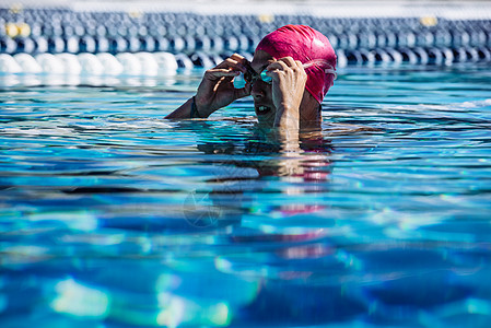 在水中游泳池扶着护目镜的游泳者图片