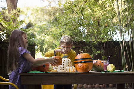 男孩和妹妹在花园桌上雕刻南瓜图片