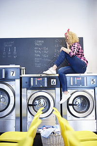 女洗衣店主坐在洗衣机顶上在黑板上写字图片