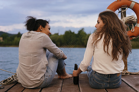 两个女人放松的坐在码头拿着啤酒瓶聊天图片