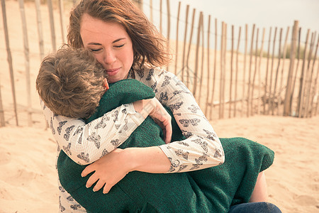 母亲在海滩上抱着裹着毯的孩子图片
