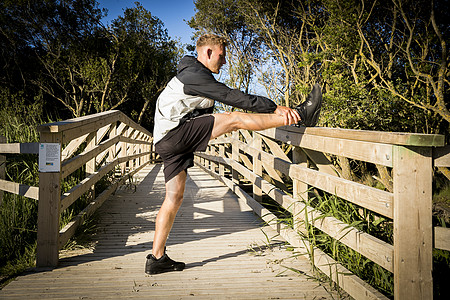 年轻男跑者在农村步行桥上伸展腿高清图片