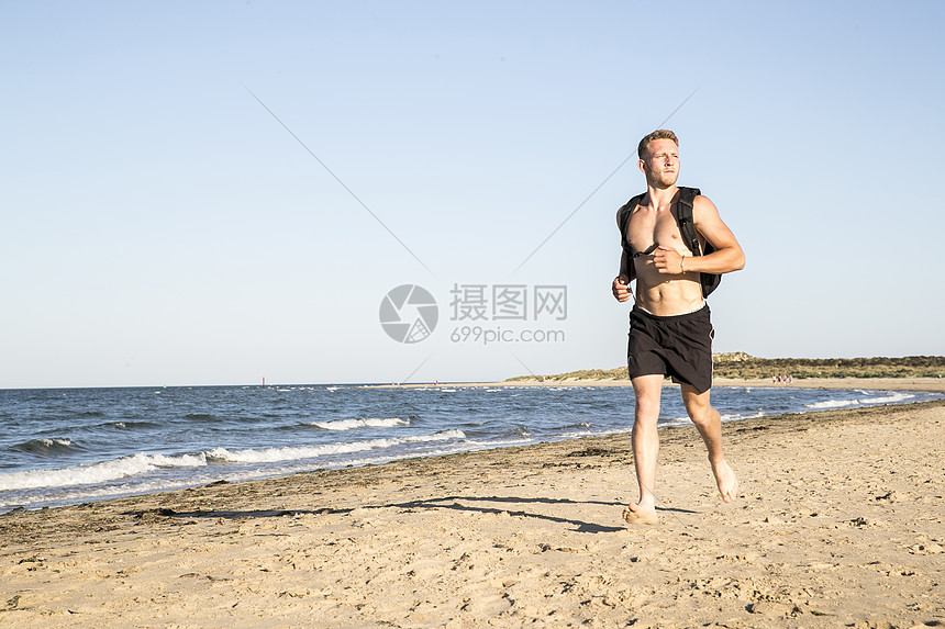 身穿短裤和背包的年轻男子跑步在海滩上图片