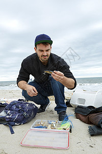 在海滩上蹲地看着钩子的年轻渔民图片