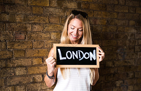 年轻女性站在砖墙前拿着伦敦的标志图片